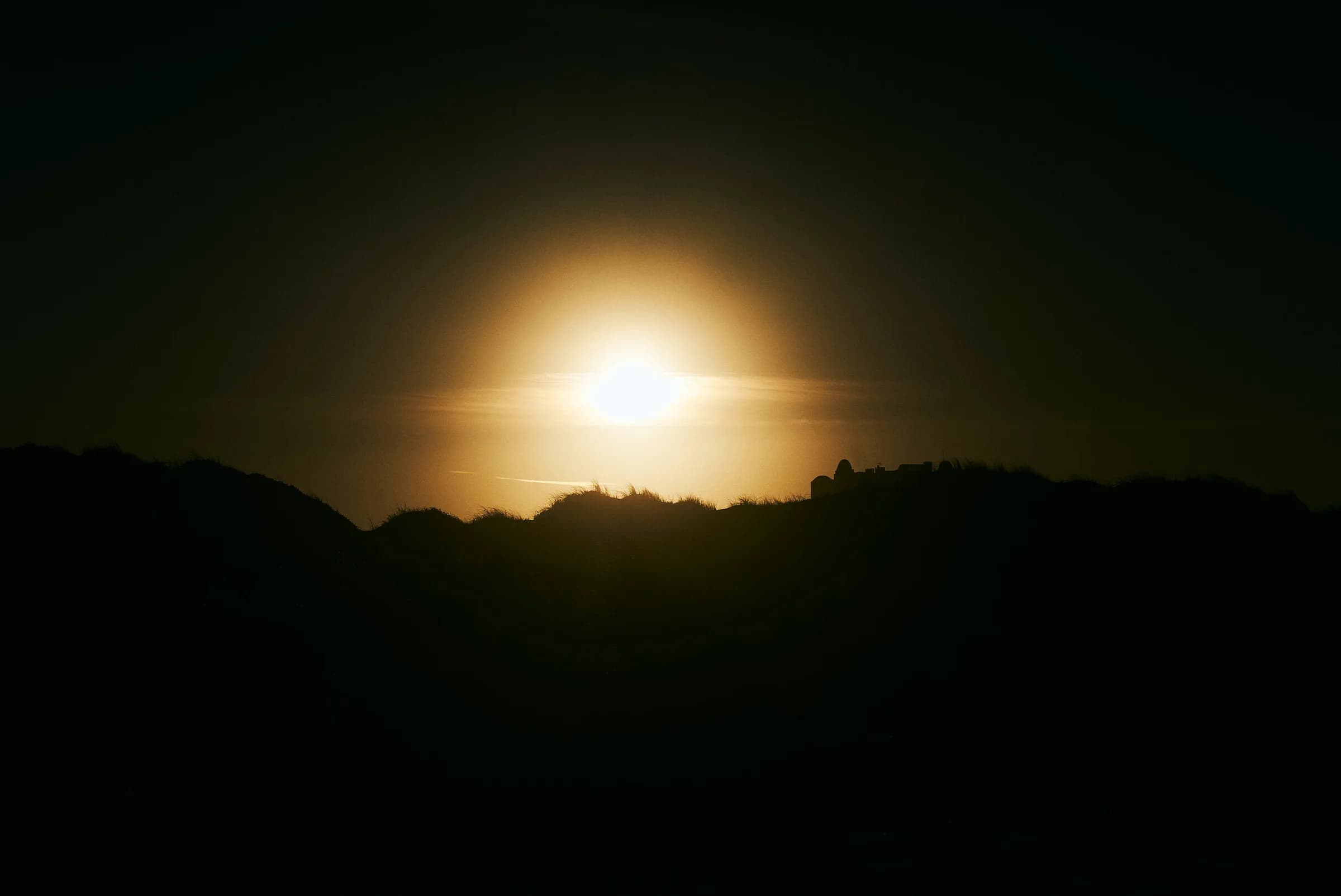 Sol velado sobre dunas en silueta