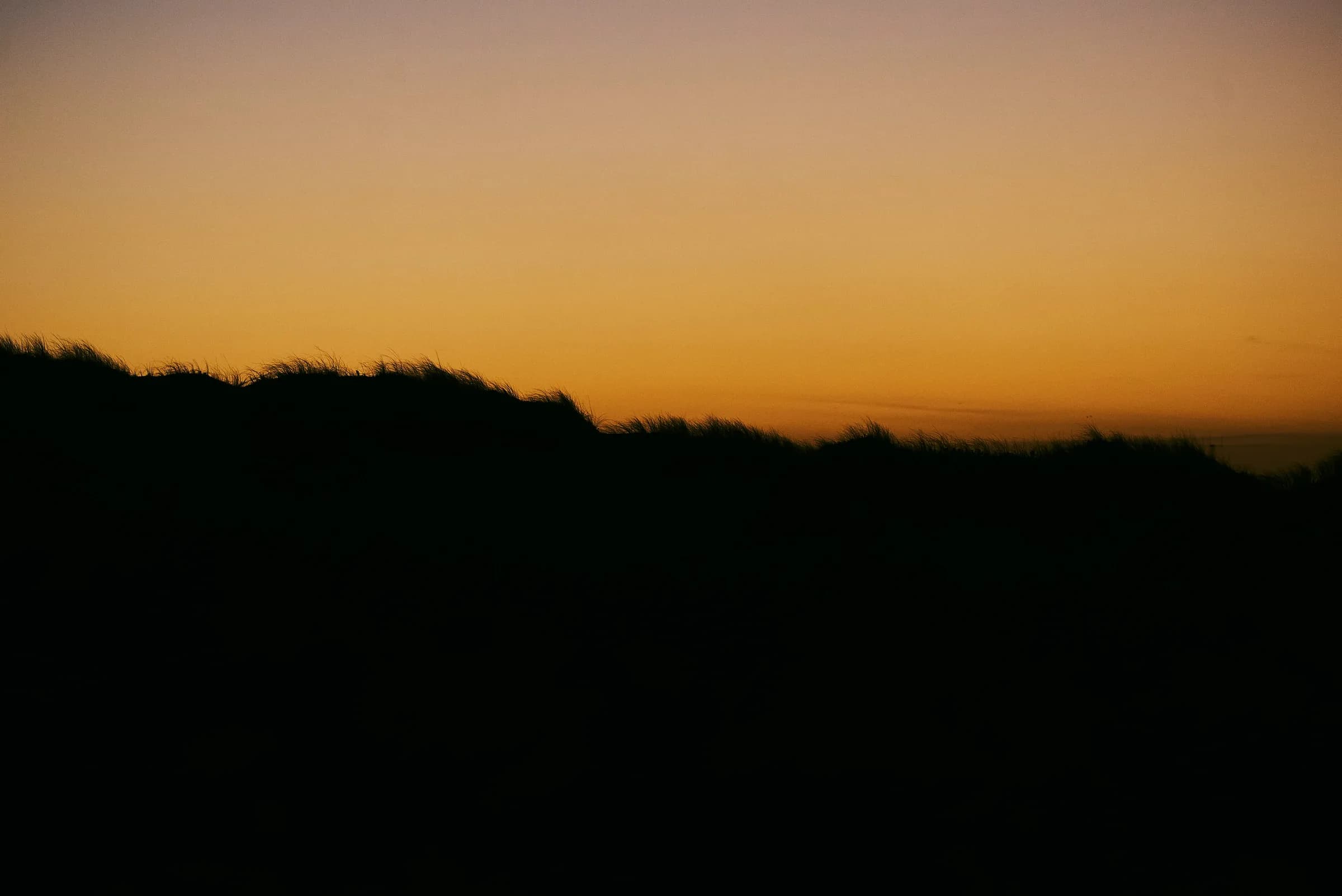 Silueta de dunas contra un cielo naranja al atardecer