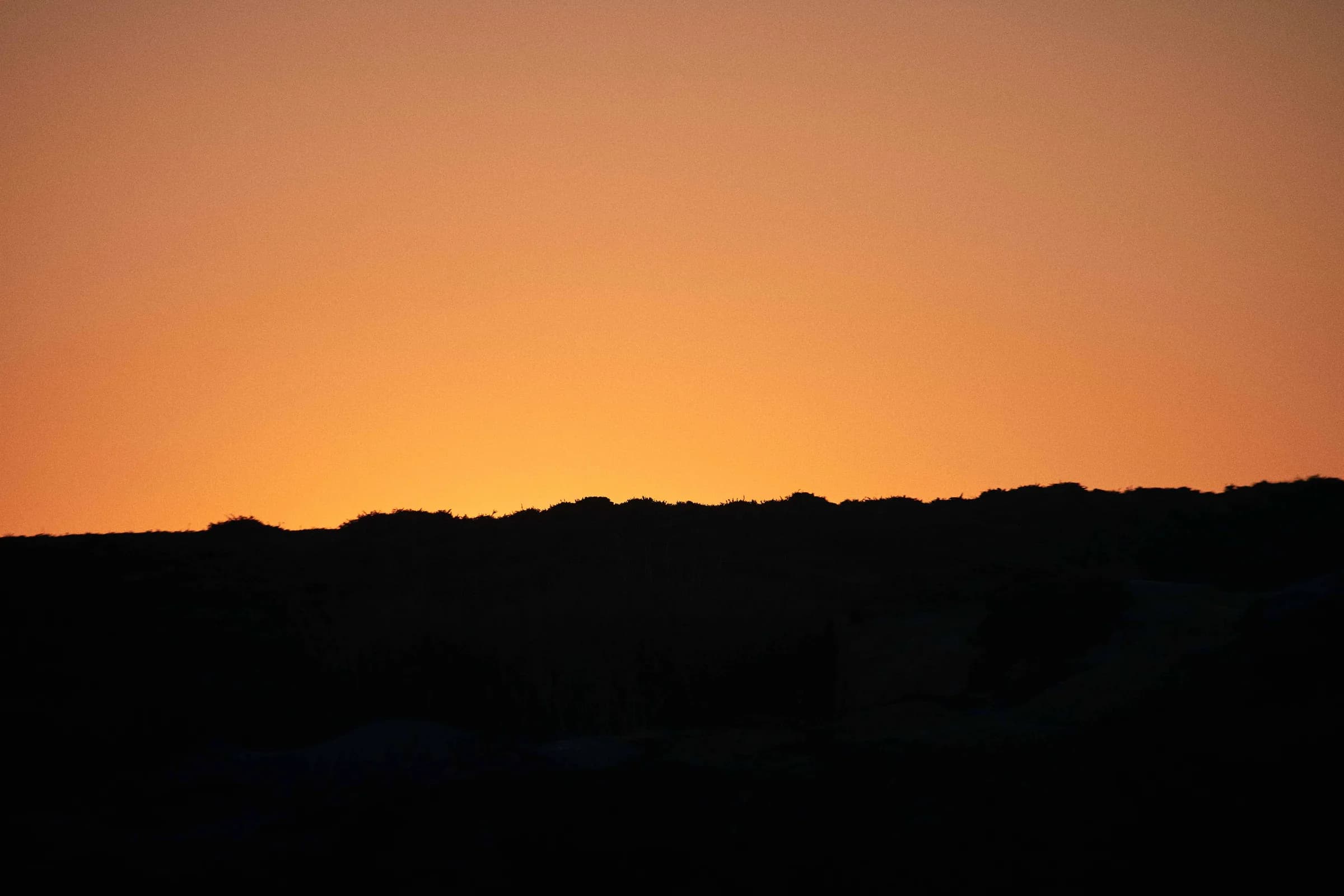 Silueta de colinas contra un cielo naranja al atardecer