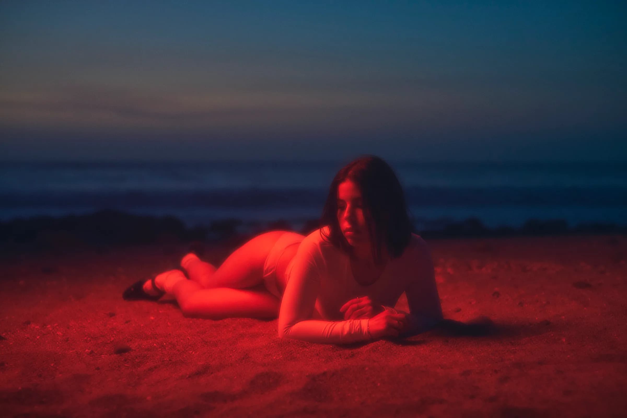 Retrato de mujer recostada en la arena bajo luz roja al anochecer