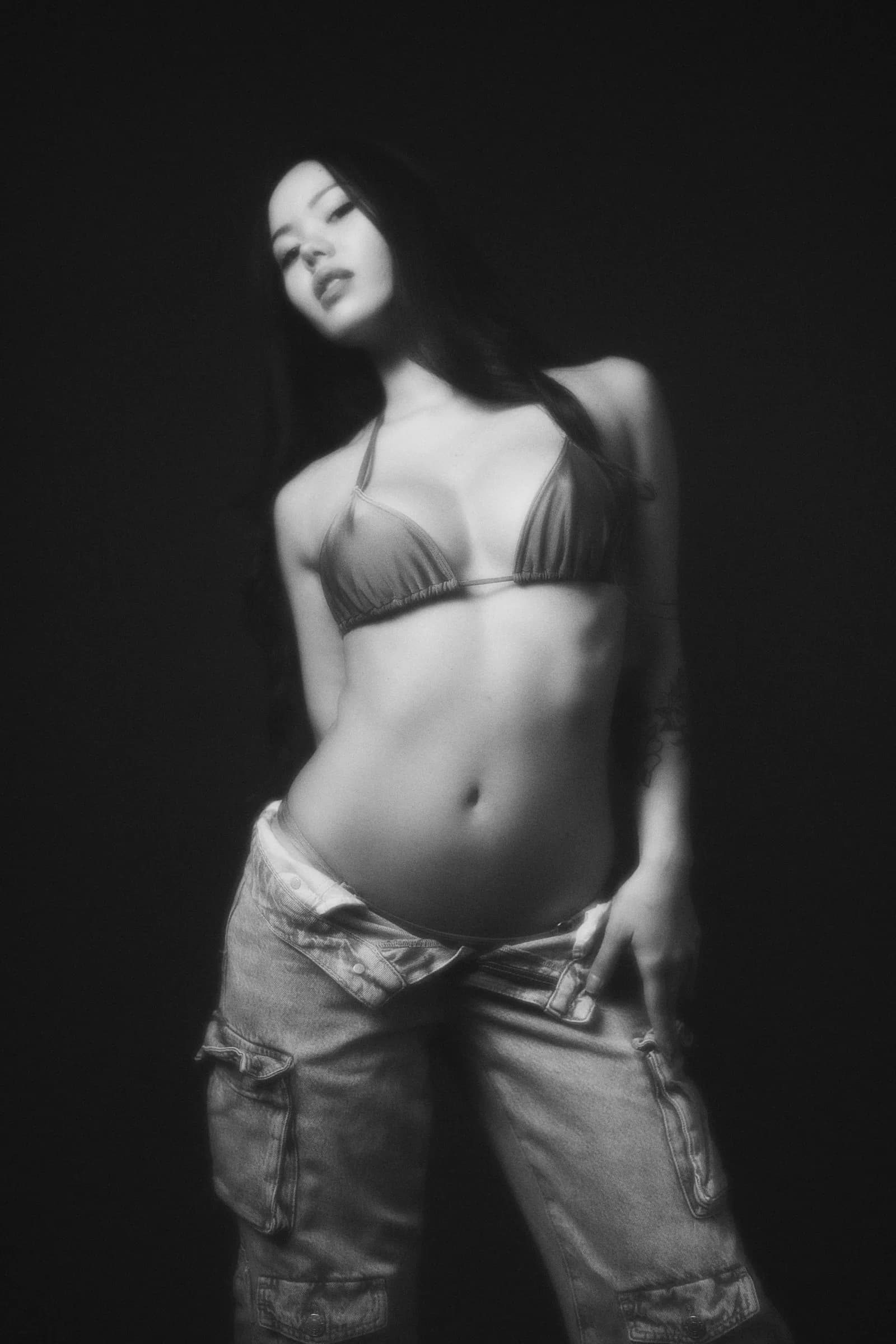 Retrato en blanco y negro de mujer con top y jeans sobre fondo negro