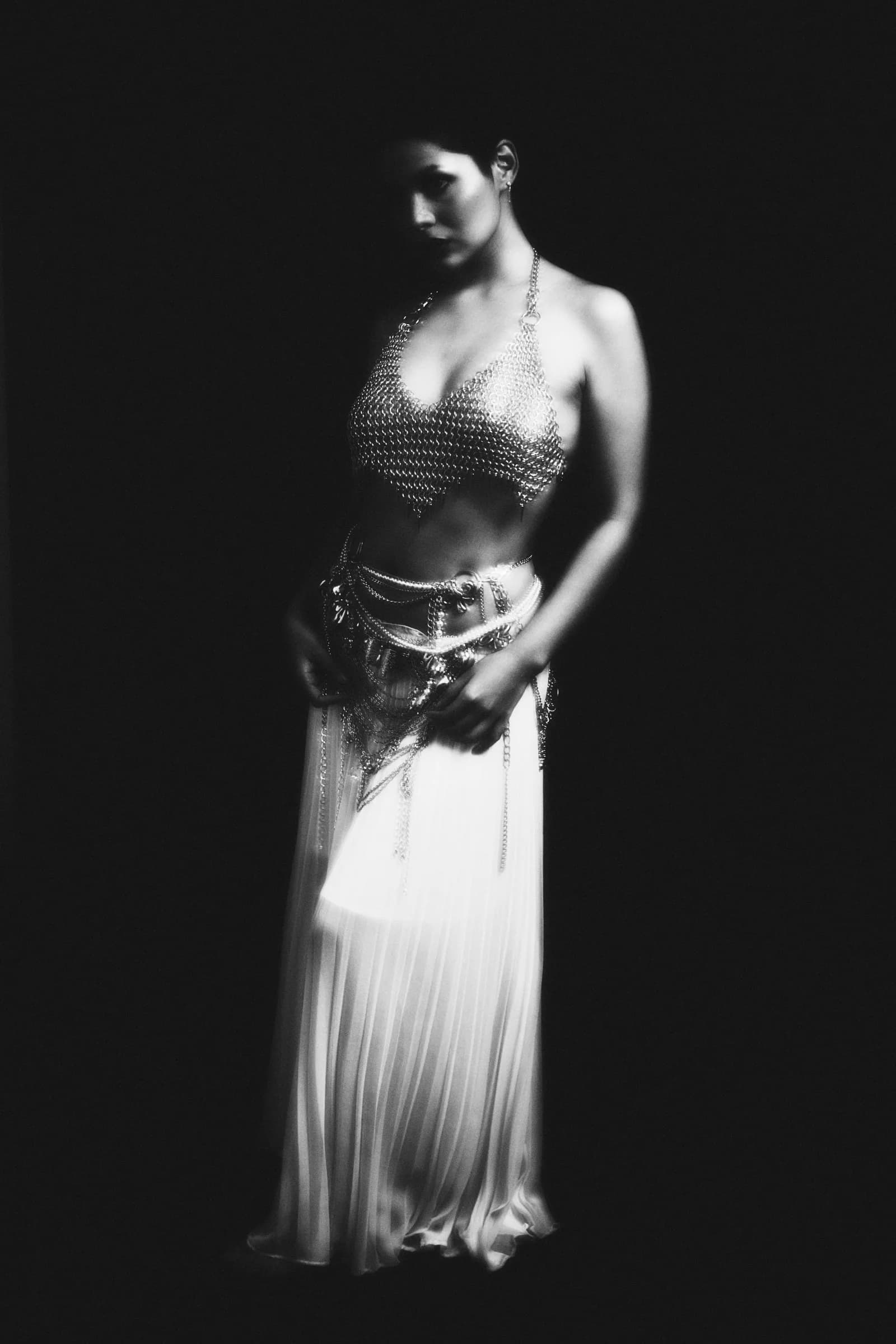 Retrato en blanco y negro de mujer con top de cota de malla y falda plisada