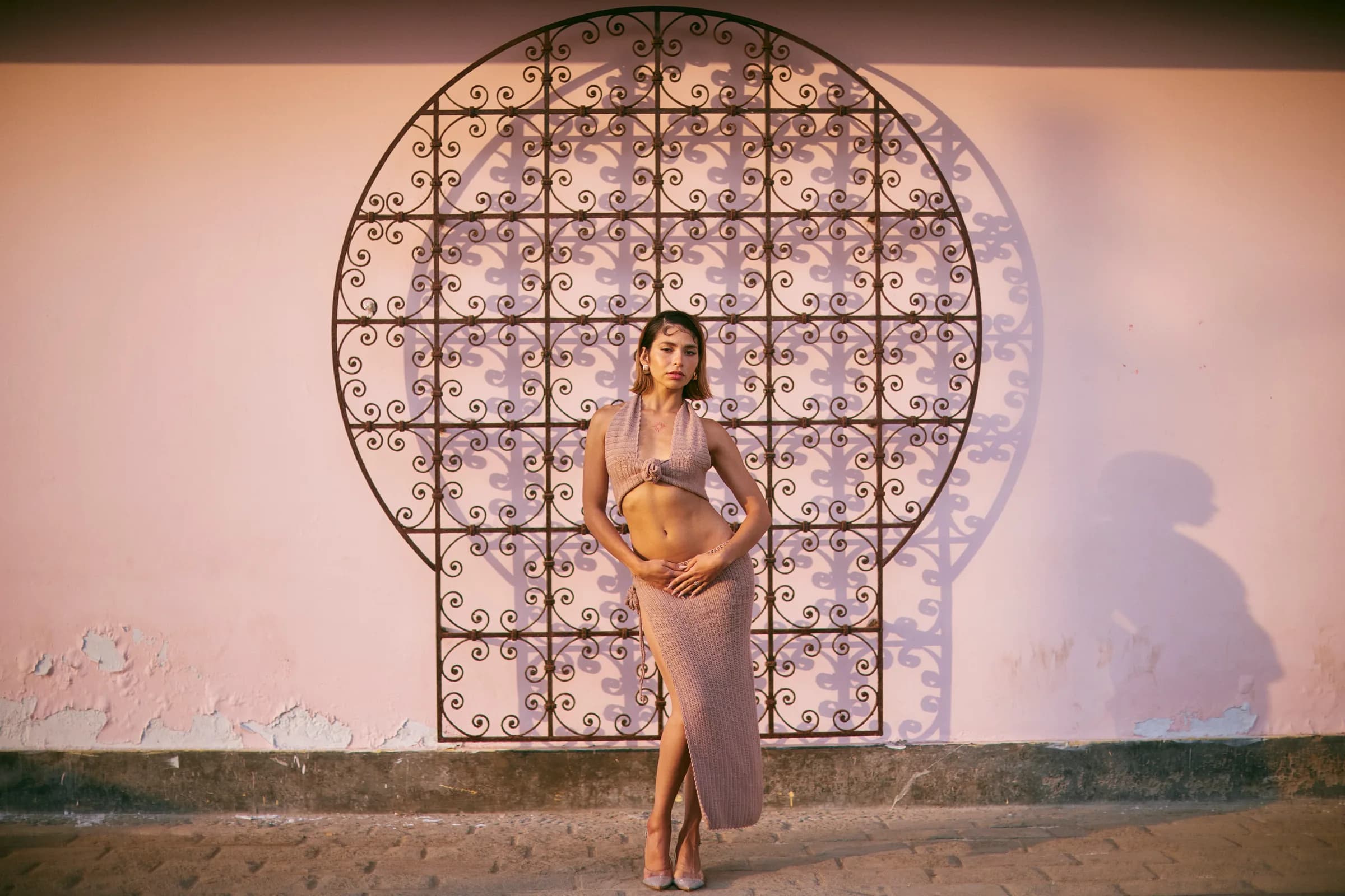 Retrato de mujer frente a una reja de hierro forjado sobre un muro rosado