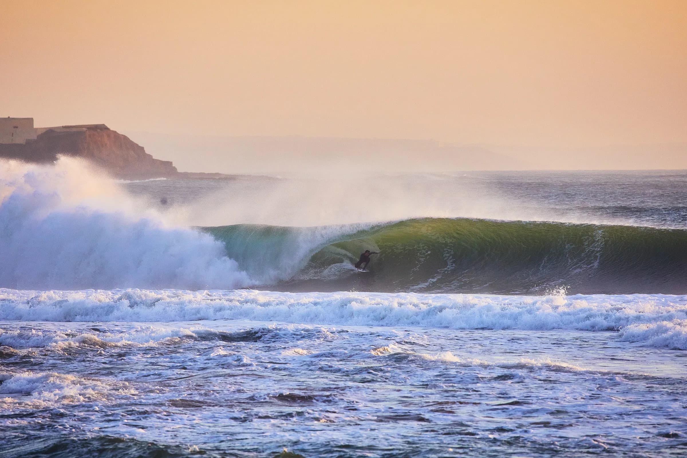 Surfista dentro del tubo de una ola al atardecer frente al acantilado