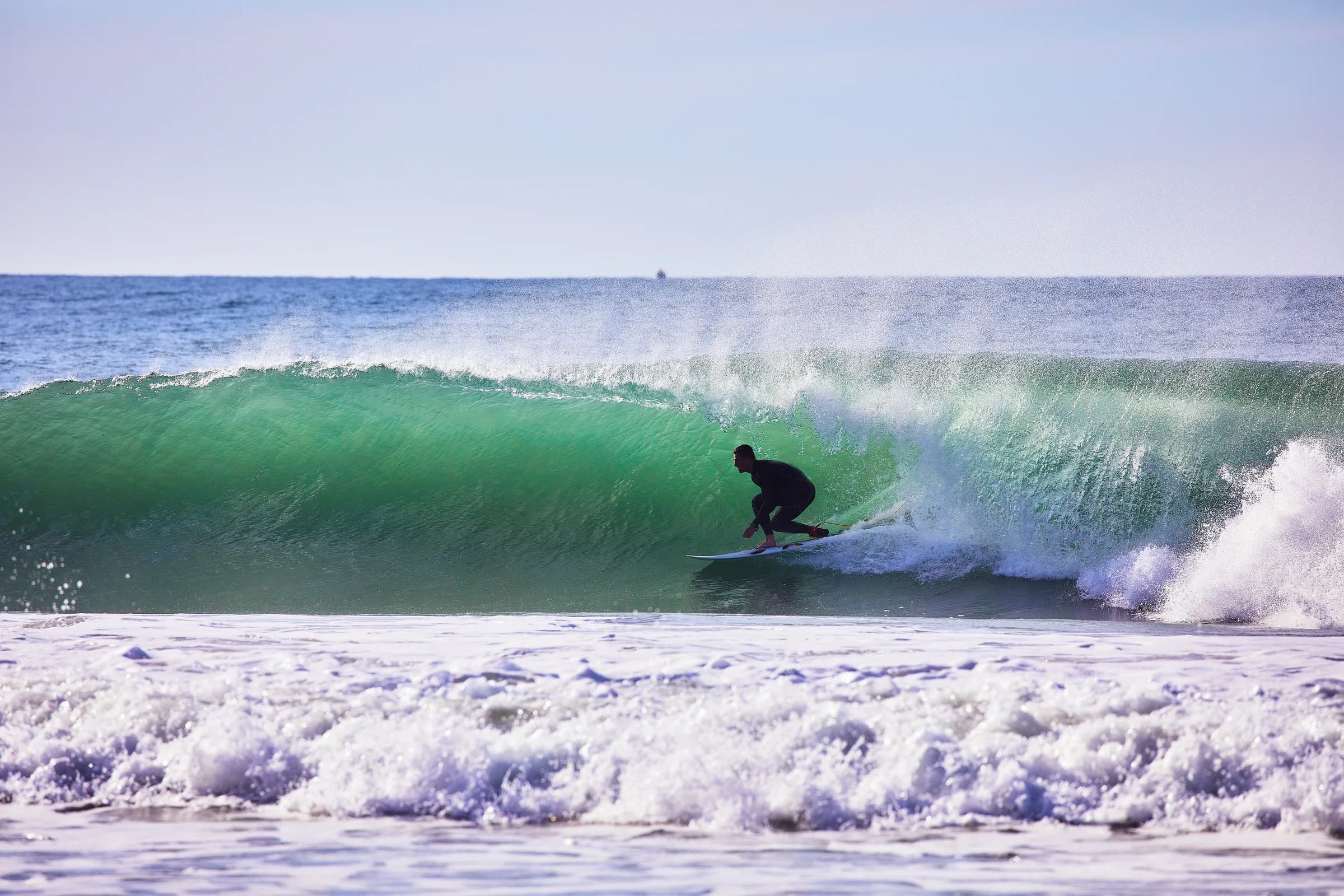 Surfista agachado dentro del tubo de una ola verde en un día despejado