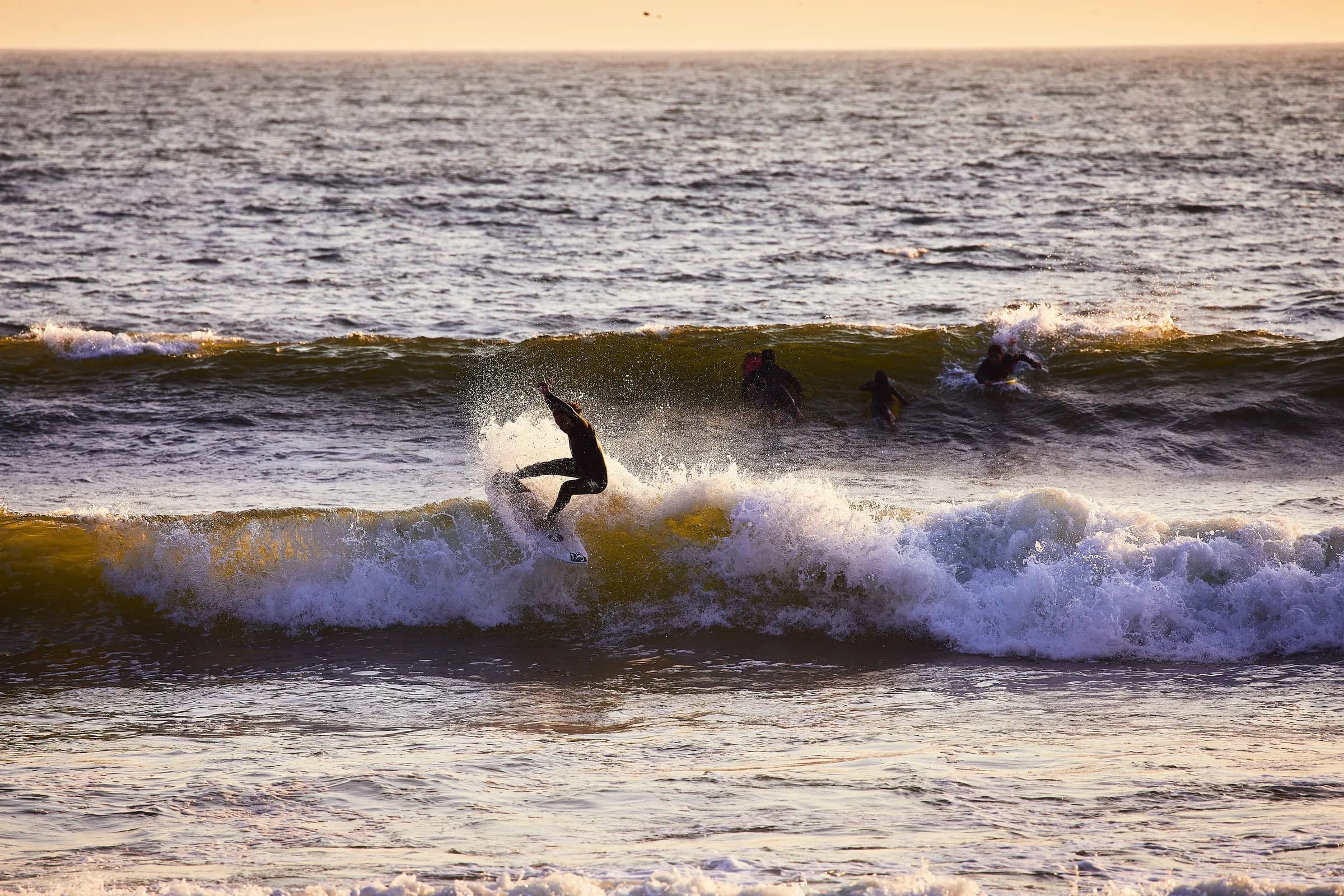 Surfista girando sobre una ola al atardecer con otros surfistas remando al fondo