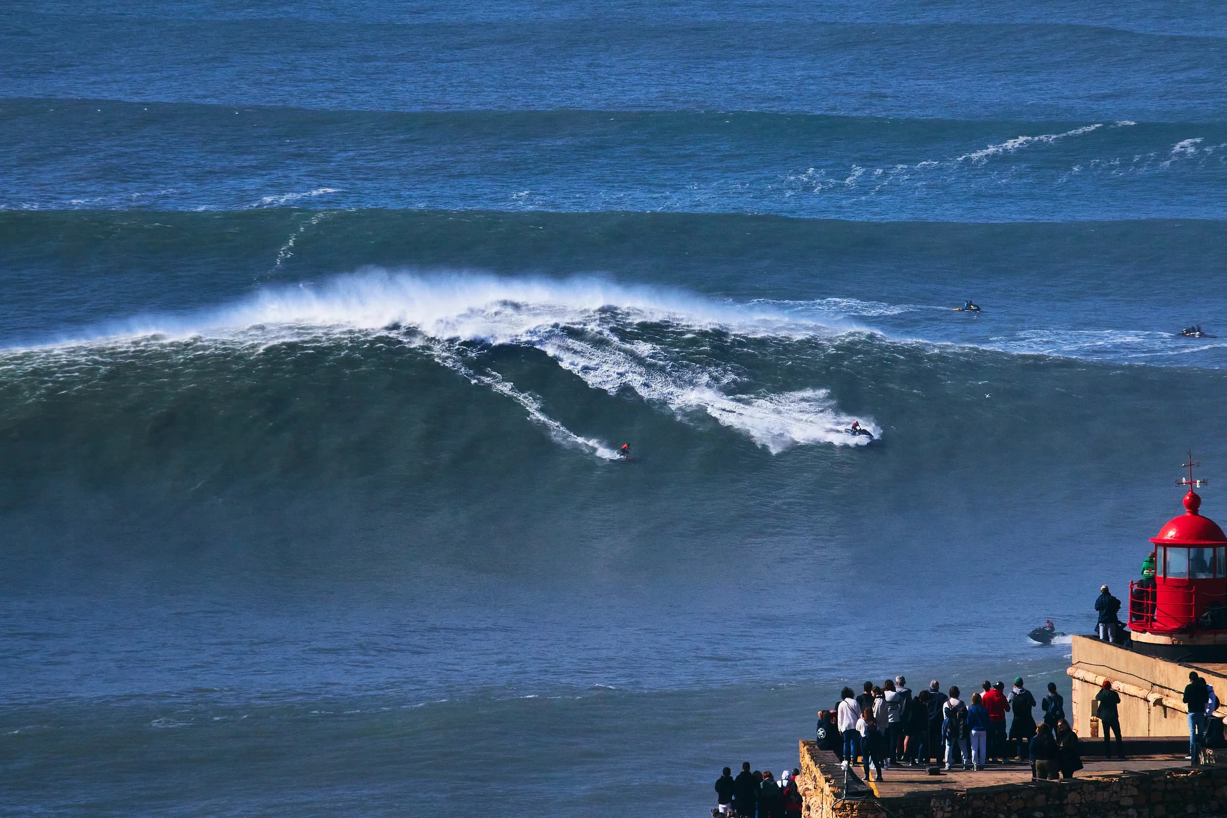 Surfista descendiendo una ola gigante en Nazaré junto al faro rojo