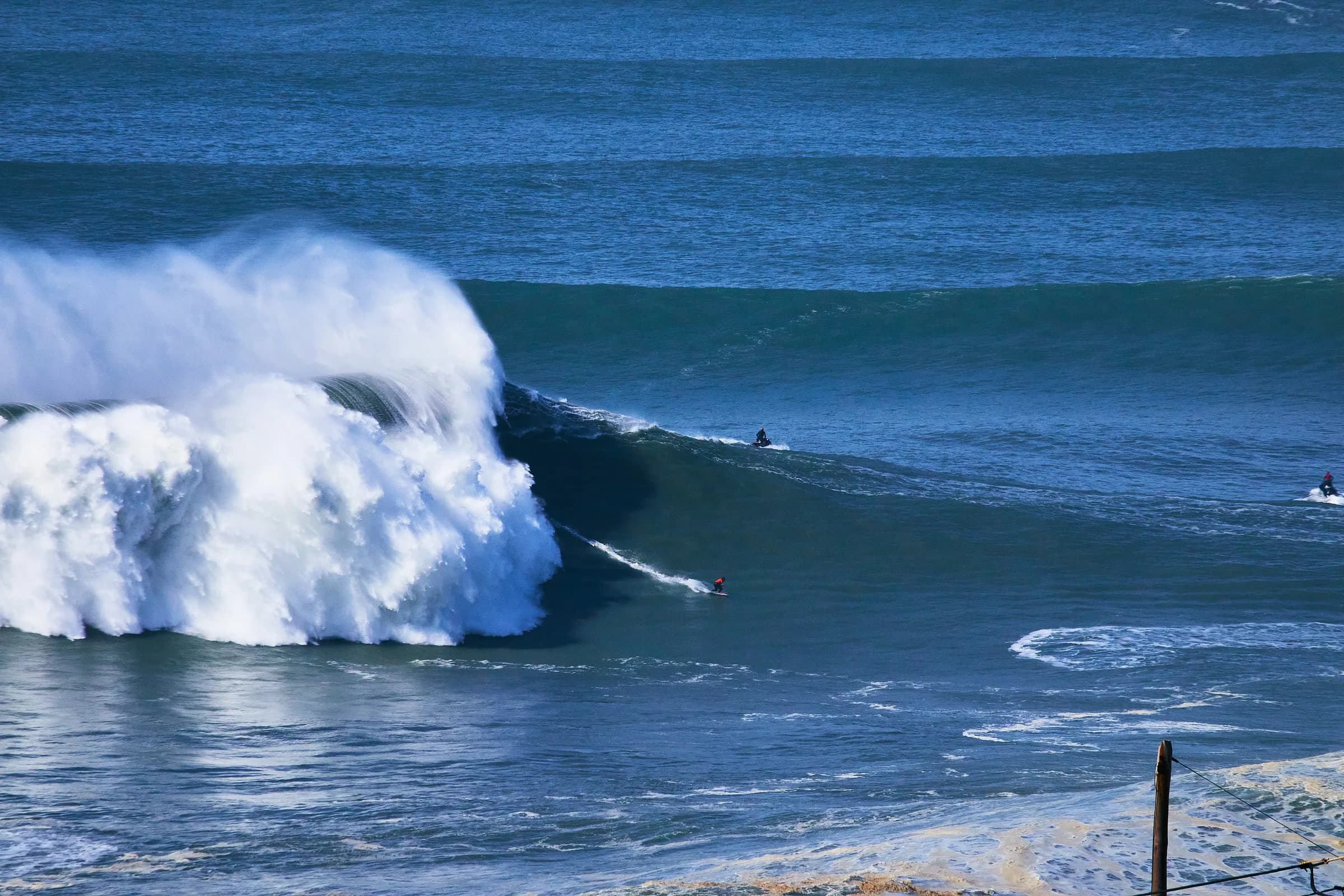 Surfista bajando una ola gigante que revienta en Nazaré