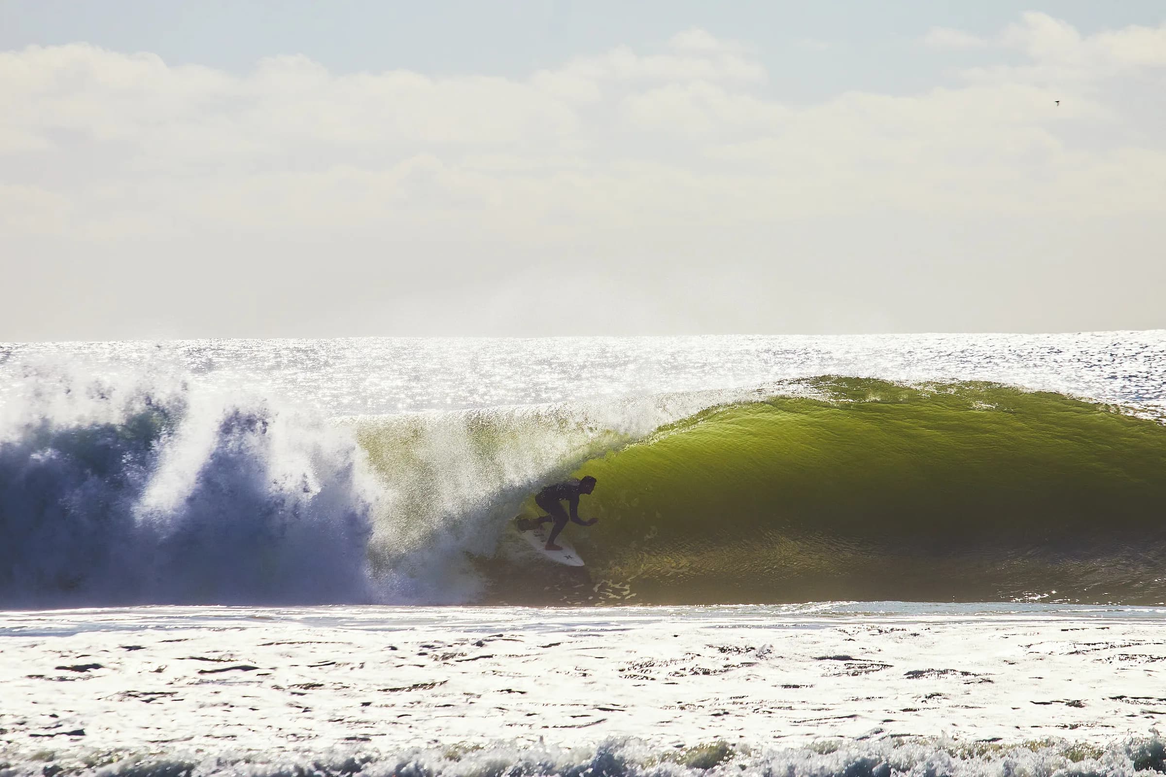 Surfista dentro de una ola verde iluminada por el sol