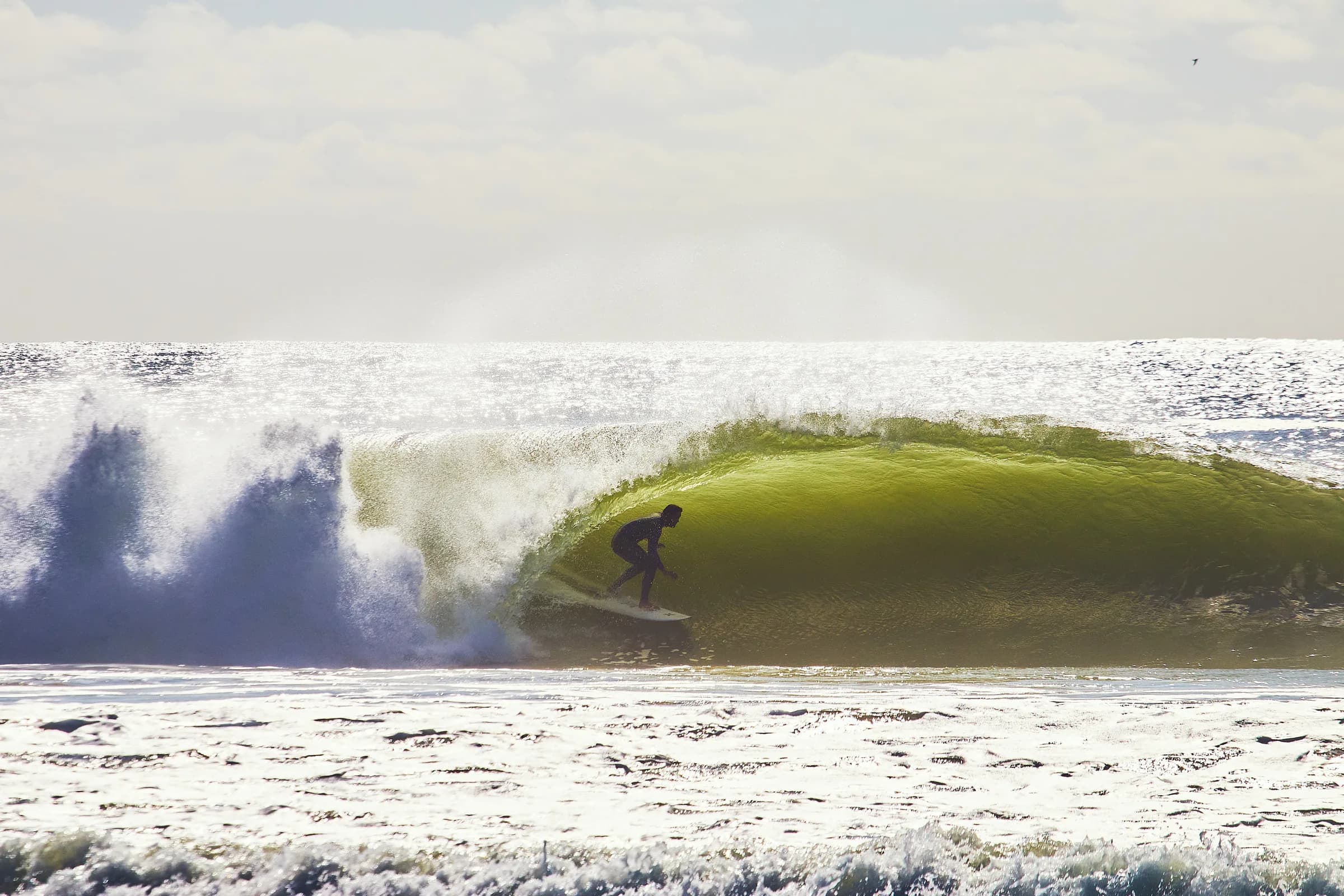 Silueta de surfista en el tubo de una ola verde a contraluz