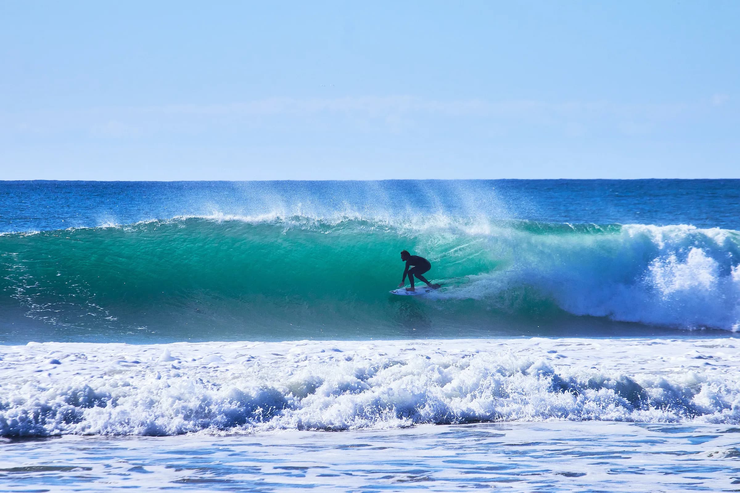 Surfista dentro del tubo de una ola turquesa en un día despejado