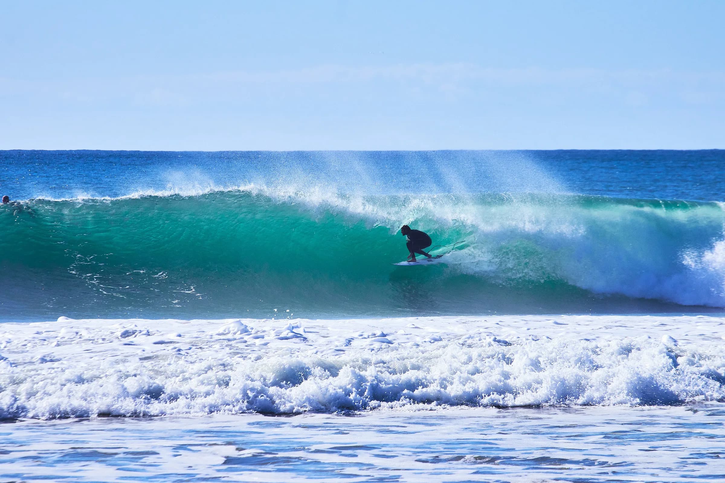 Surfista agachado dentro del tubo de una ola turquesa