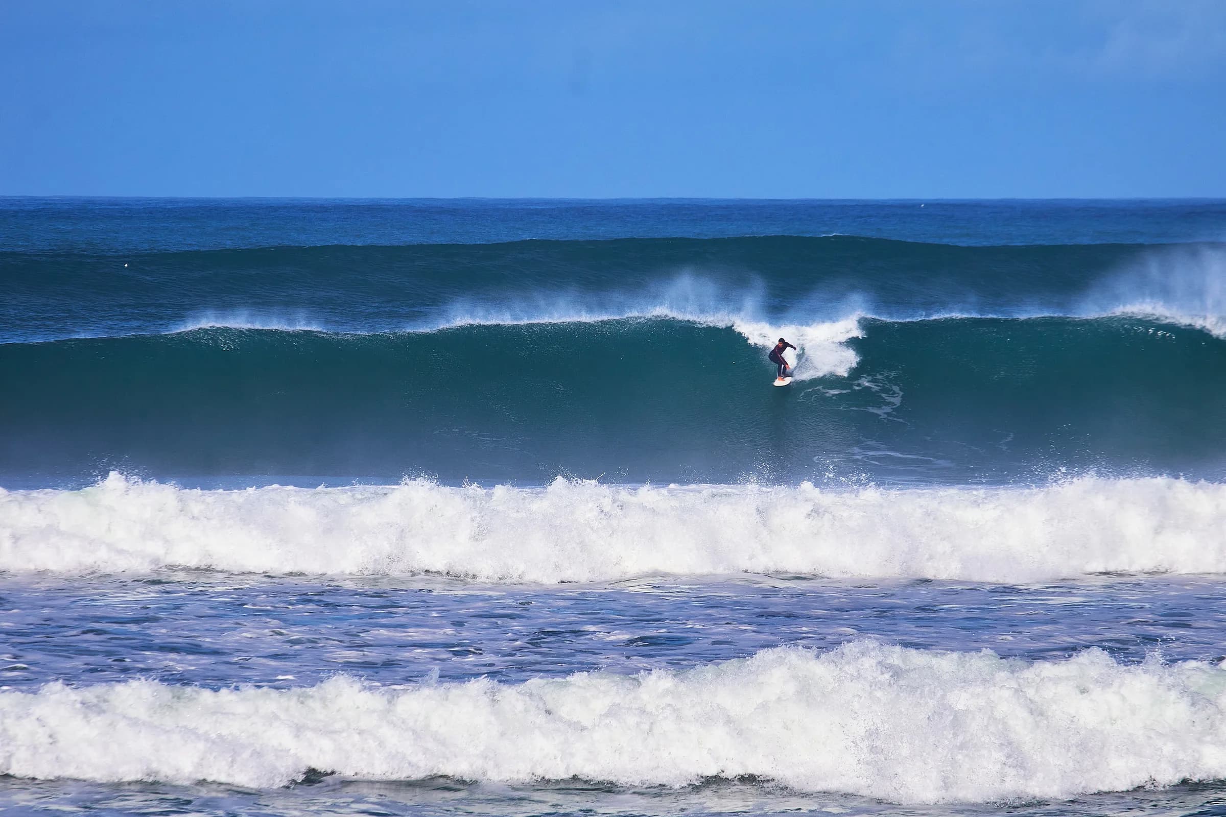 Surfista bajando una ola azul de mar abierto