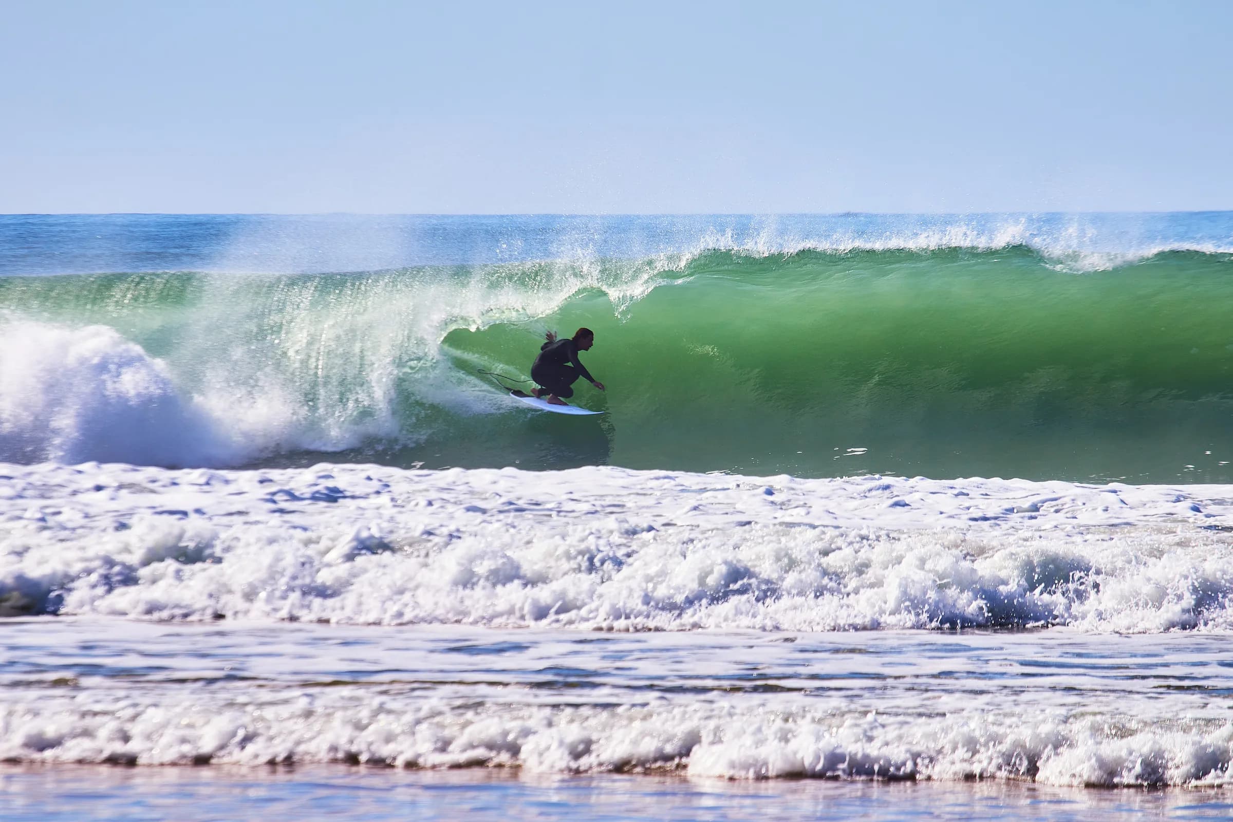 Surfista agachado dentro del tubo de una ola verde