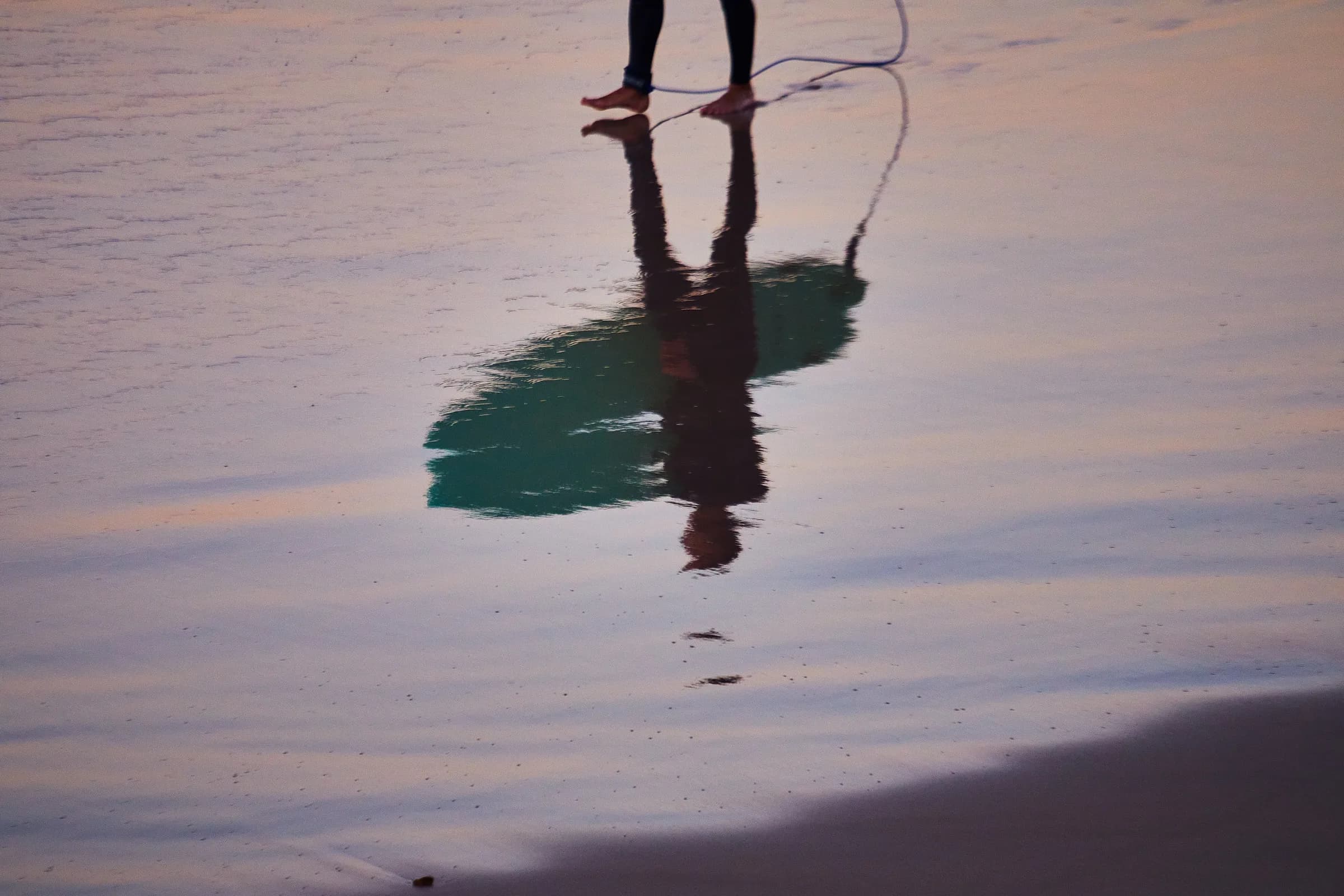 Reflejo de un surfista y su tabla en la arena mojada al atardecer