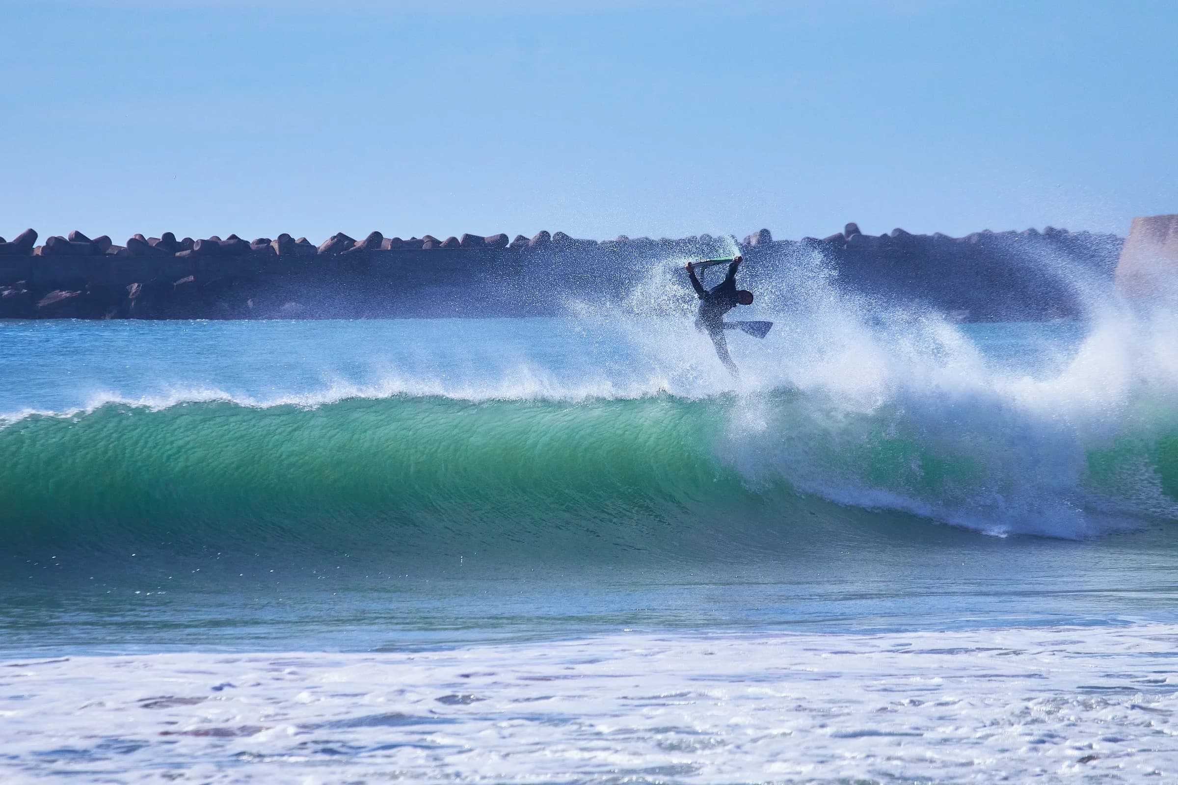Bodyboarder en el aire sobre una ola frente al rompeolas