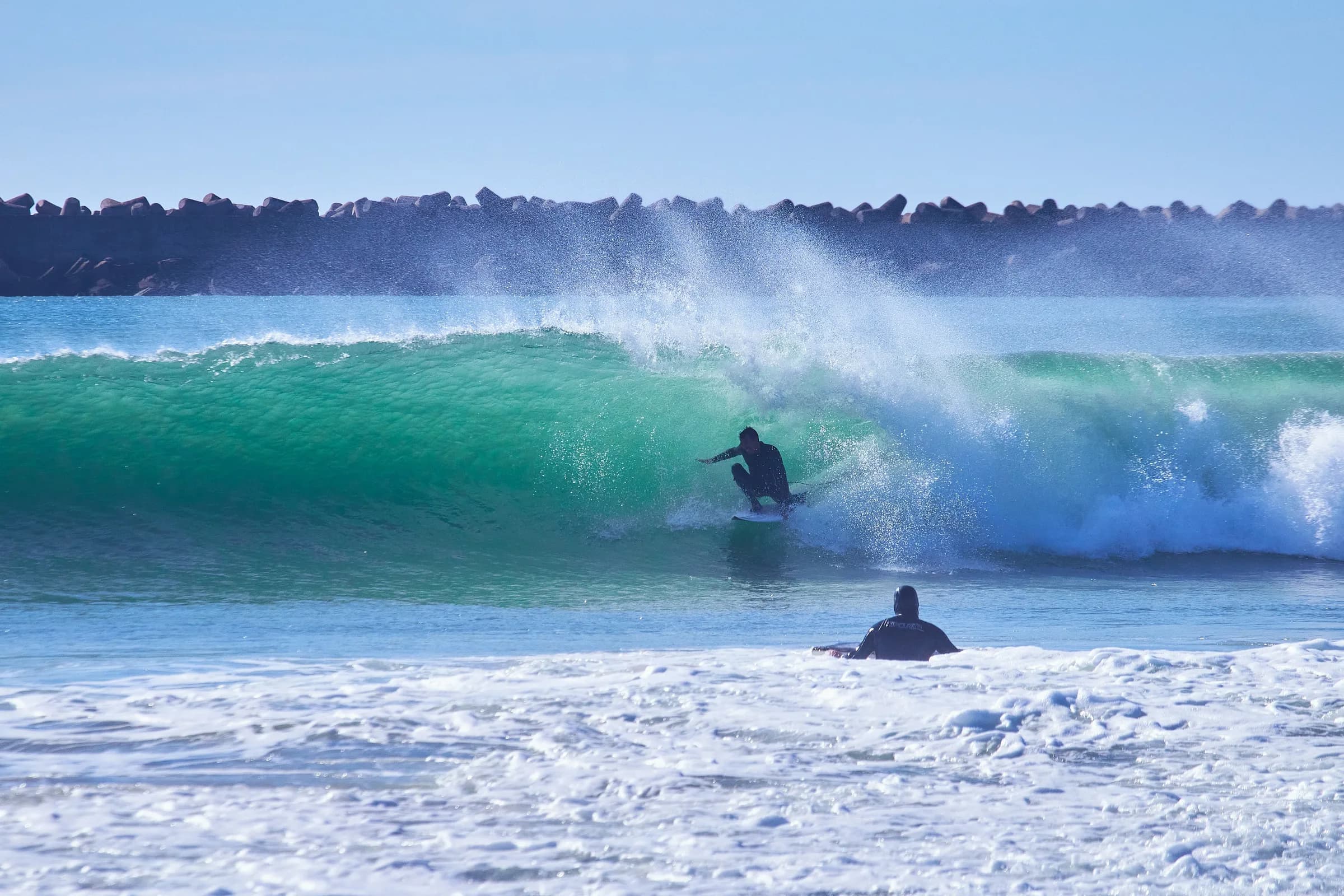 Surfista en el tubo de una ola mientras otro espera en el agua