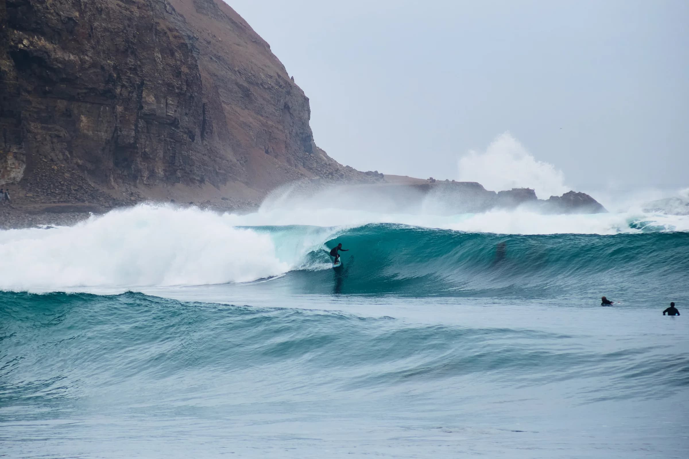 Surfista en el tubo de una ola frente a un acantilado